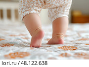 Baby taking first steps on soft quilt in a cozy bedroom setting. Малыш делает первые шаги на мягком одеяле в уютной спальне. Стоковое AI-изображение, AI-художник Katsiaryna Repich / Фотобанк Лори
