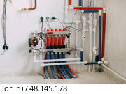 Central heating system image showing multiple red and blue pipes connected to control panel with valves and gauges. System is set up against plain wall. Underfloor heating system. Стоковое фото, фотограф Анна Маркина / Фотобанк Лори