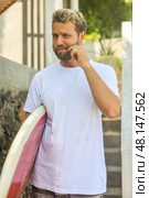 A Young Man Embracing a Surfing Lifestyle with His Surfboard in a Vibrant Tropical Environment. Стоковое фото, фотограф Женя Канашкин / Фотобанк Лори