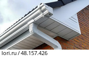 The white aluminum guttering is beautifully installed alongside a brick wall with a downpipe, showcasing a modern yet classic home exterior. Стоковое AI-изображение, AI-художник Данила Большаков / Фотобанк Лори