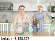 Young girl cleaning the table surface, mother vacuum-cleaning in the kitchen. Стоковое фото, фотограф Яков Филимонов / Фотобанк Лори