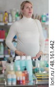 Interested pregnant woman in white sweater browsing store shelves, thoughtfully selecting household products while shopping for home essentials. Стоковое видео, видеограф Яков Филимонов / Фотобанк Лори