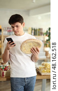 Interested smiling(focused) young guy using mobile app to scan frozen cheese pizza for discounts and promotional offers during shopping in grocery store. Стоковое видео, видеограф Яков Филимонов / Фотобанк Лори