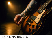 Ink-covered guitarist prepares vintage hollow-body electric for soulful evening gig illuminated by warm amber stage light and smoky ambience. Стоковое AI-изображение, AI-художник Павел Муравьев / Фотобанк Лори