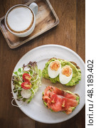 Delicious breakfast featuring avocado toast and smoked salmon with coffee on a wooden table, flatlay. Стоковое фото, фотограф Владимир Разгуляев / Фотобанк Лори