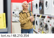 Elderly man choosing washing machine in showroom of electrical appliance store. Стоковое фото, фотограф Татьяна Яцевич / Фотобанк Лори