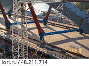 The construction of a bridge is underway with a white crane standing tall in the center of the image, supporting the steel beams overhead. Стоковое фото, фотограф Данила Большаков / Фотобанк Лори