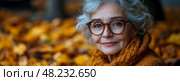 A kind-hearted elderly woman with gray curly hair sits among vibrant autumn leaves, wearing glasses and a cozy sweater, radiating warmth and joy. Стоковое AI-изображение, AI-художник Данила Большаков / Фотобанк Лори
