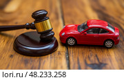 A small red toy car rests beside a gavel on a rustic wooden table, representing legal issues and disputes related to automobiles and traffic laws. Стоковое AI-изображение, AI-художник Данила Большаков / Фотобанк Лори