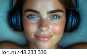 A young woman with blue eyes and freckles relaxes, listening to music through headphones while smiling contentedly in her calm indoor space. Стоковое AI-изображение, AI-художник Данила Большаков / Фотобанк Лори