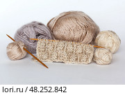 Close-up of accessories for hand knitting - balls and skeins of wool and acrylic yarn and the beginning of knit a soft scarf with a voluminous pattern on wooden knitting needles on white background. Стоковое фото, фотограф Виктория Катьянова / Фотобанк Лори
