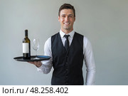 Waiter with a tray on which there is a bottle of wine and an empty glass. Стоковое AI-изображение, AI-художник Дмитрий Киселёв / Фотобанк Лори