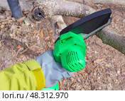 Ручная портативная электрическая пила на аккумуляторе для распиловки дров и древесины. Hand-held portable  electric saw on a battery for cutting firewood and wood. Close-up, a hand sawing a log. Стоковое фото, фотограф Татьяна Д / Фотобанк Лори