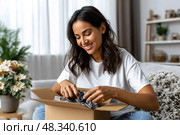 A woman is sitting on a couch and opening a box. Стоковое фото, фотограф Ярославский Максим / Фотобанк Лори