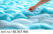 A hand gently explores the inviting, wavy surface of light blue foam, creating a calming atmosphere in a tranquil indoor space. Стоковое AI-изображение, AI-художник Данила Большаков / Фотобанк Лори