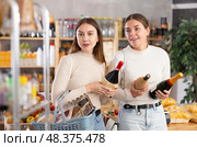 Two girls in store while shopping, choose bottle of wine and chat sweetly. Стоковое фото, фотограф Яков Филимонов / Фотобанк Лори