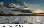 Sunset over the lake. The sky is orange on the horizon. The sun is shining from behind the clouds. Golden backlight. Silhouettes of hills in the distance. Ripples on the water. Madagascar. Mantasoa. Стоковое фото, фотограф Вера Ивановна Кубарева / Фотобанк Лори
