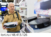 Senor man pensioner buying Robotic vacuum cleaner in showroom of electrical appliance store. Стоковое фото, фотограф Татьяна Яцевич / Фотобанк Лори