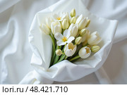 Нежный букет воздушных цветов, лепестки которых мерцают, словно лунный свет, нежно обернут в полупрозрачную белую ткань. A delicate bouquet of airy flowers, the petals of which shimmer like moonlight, are gently wrapped in translucent white fabric. Стоковое AI-изображение, AI-художник Наталия Ануфриева / Фотобанк Лори
