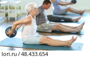 Sitting on floor, mature woman with class participants move soft ball around torso. Стоковое видео, видеограф Яков Филимонов / Фотобанк Лори