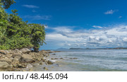 Boulders are scattered on the rocky coast of the turquoise ocean. Green tropical trees against a background of blue sky, clouds. Mountains on the horizon. A sunny day. Malaysia. Borneo. Kota Kinabalu. Стоковое фото, фотограф Вера Ивановна Кубарева / Фотобанк Лори