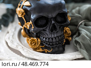 A mysterious black skull with golden roses and pumpkins on serving plates for a Halloween or Day of the Dead party. Стоковое фото, фотограф Photojuli / Фотобанк Лори