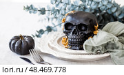 A mysterious black skull with golden roses and pumpkins on serving plates for a Halloween or Day of the Dead party. Стоковое фото, фотограф Photojuli / Фотобанк Лори