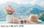 Summer day concept: pink flowers in a vase, drink in glass jar, glasses, a sunhat on a light table with blurred hillscape in the sunny day for poster, print. Стоковое AI-изображение, AI-художник Данила Большаков / Фотобанк Лори