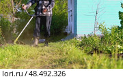 Gardener with grass trimmer mows lawn. Стоковое видео, видеограф Igor Skripachev / Фотобанк Лори
