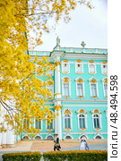 Russia, St. Petersburg, 10 May 2025: the incredibly picturesque facade of the Winter Palace through the branches of trees on a clear spring day, actors in tsarist outfits, the heritage of Russia. Редакционное фото, фотограф Vladimir Drozdin / Фотобанк Лори