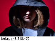 A teenage girl in a black hoodie with a hood on a red background. The face is closed. The concept of problems in adolescents and the difficulties of the transition period. Portrait Close-up. Стоковое фото, фотограф Луиза Налимова / Фотобанк Лори