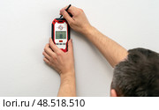 Man using stud finder to locate framing studs located behind the walling surface. Using a wall scanner to identify hidden electrical wiring. Space for text. Стоковое фото, фотограф Луиза Налимова / Фотобанк Лори