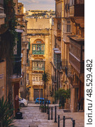 VALLETTA, MALTA - NOVEMBER 12, 2018 - Hilly ancient streets view with colourful balconies, people and cars in the medieval city. Стоковое фото, фотограф Сергей Богомяко / Фотобанк Лори
