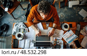 A man is busily typing on a laptop amidst a chaotic assortment of papers, books, and office supplies, suggesting a productive yet disorganized workspace. Стоковое AI-изображение, AI-художник Данила Большаков / Фотобанк Лори
