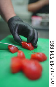 Professional chef in black gloves slicing ripe red tomatoes on green cutting board with sharp knife during culinary food preparation in commercial kitchen workspace. Стоковое видео, видеограф Данил Руденко / Фотобанк Лори