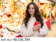 Cheerful woman with paper cup of hot tea walking at Christmas street fair. Стоковое фото, фотограф Яков Филимонов / Фотобанк Лори