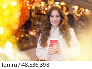 Cheerful woman with paper cup of hot tea walking at Christmas street fair. Стоковое фото, фотограф Яков Филимонов / Фотобанк Лори