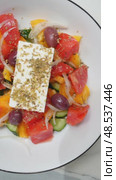 Fresh Greek salad ingredients layering into white bowl, combining tomatoes, cucumbers, feta, salmon, olives, arugula, avocado cream, croutons, sunflower seeds. Стоковое видео, видеограф Данил Руденко / Фотобанк Лори