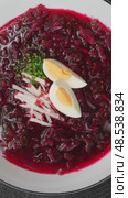 Red borscht soup is garnished with boiled egg, fresh herbs, and radish slices, served in white bowls on a black placemat with sour cream and lemon wedges on the side. Стоковое видео, видеограф Данил Руденко / Фотобанк Лори