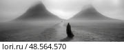 Two cloaked figures traverse a misty expanse, heading towards dark hills shrouded in fog under the quiet light of early morning. Стоковое AI-изображение, AI-художник Данила Большаков / Фотобанк Лори