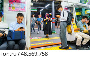 Tokyo, Japan - Sep 30 2024, Panoramic view of male and female passengers standing and sitting in a Tokyo JR subway van, a boy standing on a corner, with door open to platform, at night, Tokyo, Japan. Редакционное фото, фотограф Сергей Богомяко / Фотобанк Лори