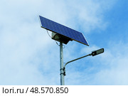Уличный фонарь на солнечных батареях, установленный на высоком металлическом столбе и слегка наклоненный вверх для максимального поглощения солнечного света. Концепция интеграции солнечной энергии в повседневную инфраструктуру. Стоковое фото, фотограф Дарья Савченко / Фотобанк Лори