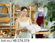 Cute young girl customer holding box with decorative bow and buying sweet authors flour products in bakery shop. Стоковое фото, фотограф Яков Филимонов / Фотобанк Лори