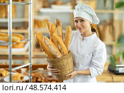 Positive young woman baker in white uniform baking fresh baguettes in bakery. Стоковое фото, фотограф Яков Филимонов / Фотобанк Лори