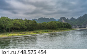 The landscape of a beautiful calm river. Ripples on the shiny water. Green vegetation on the shore. Picturesque mountains against the sky and clouds. China. Li River. Li Jiang. Guilin. Стоковое фото, фотограф Вера Ивановна Кубарева / Фотобанк Лори
