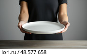 Woman serving a dish of homemade food at a dining table in a modern setting during a cozy gathering. Женщина подает блюдо с домашней едой за обеденным столом в современной обстановке во время уютной посиделки. Стоковое AI-изображение, AI-художник Katsiaryna Repich / Фотобанк Лори