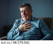 Senior man suffering chest pain while sitting on sofa at home. Стоковое AI-изображение, AI-художник Юрий Поздников / Фотобанк Лори