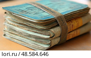 A stack of old travel documents bound together with a rubber band rests on a wooden table, showcasing a nostalgic moment in time. Стоковое AI-изображение, AI-художник Данила Большаков / Фотобанк Лори