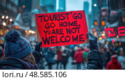 In a bustling city during winter, an individual displays a sign protesting against tourists, capturing the crowd's attention with a clear message. Стоковое AI-изображение, AI-художник Данила Большаков / Фотобанк Лори