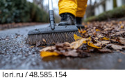 A person in yellow rain gear sweeps wet leaves off a sidewalk during a rainy day in a quiet residential neighborhood. Стоковое AI-изображение, AI-художник Данила Большаков / Фотобанк Лори